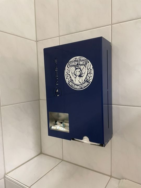 Zu sehen ist ein Spenderautomat für Menstruationsprodukte in blau mit einem weißen Logo der Soroptimisten International.